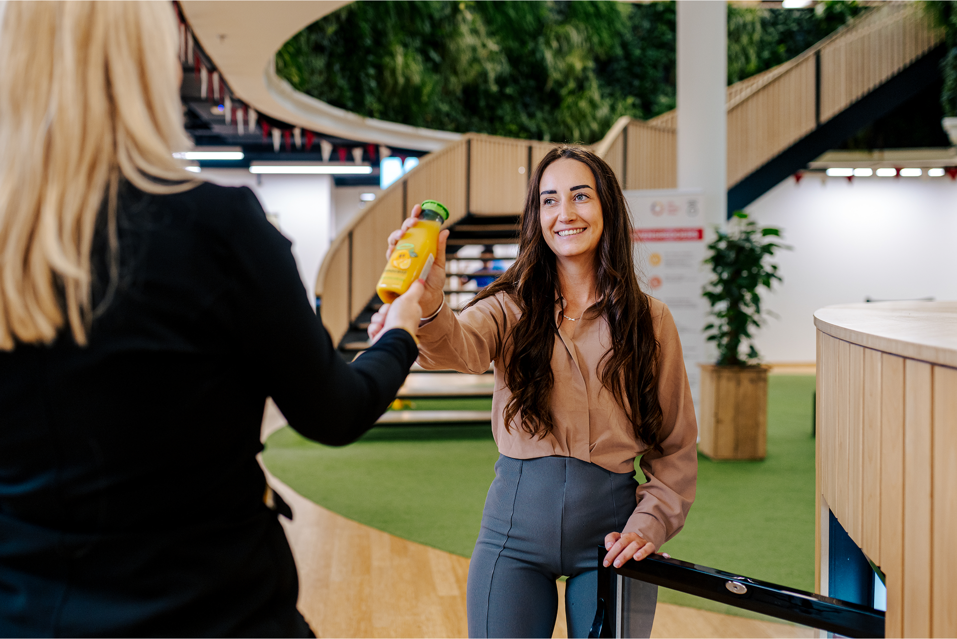 Woman handing a bottle of juice to another person.