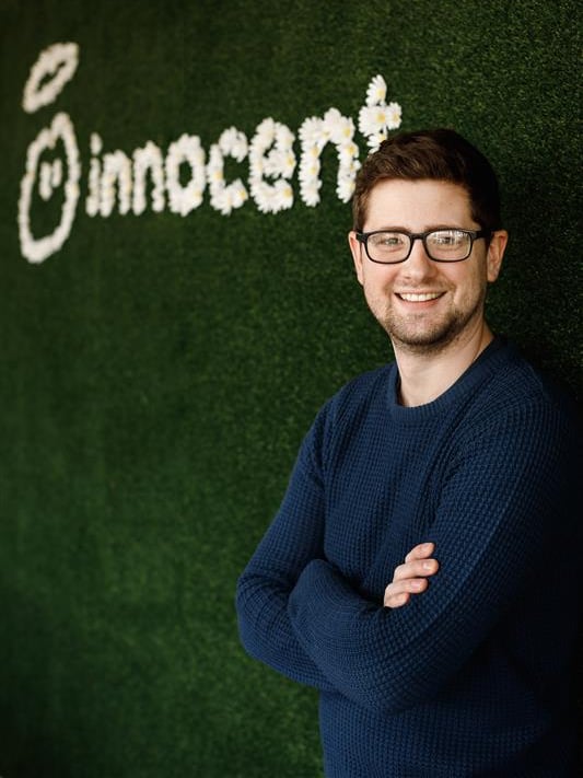 Man with glasses smiling in front of an "innocent" sign made of flowers.
