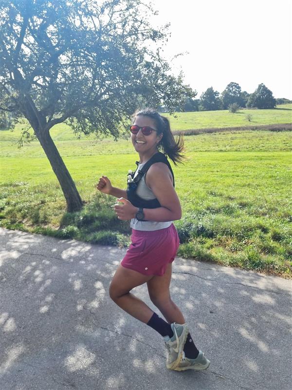 A woman running on a path with a field and trees in the background.