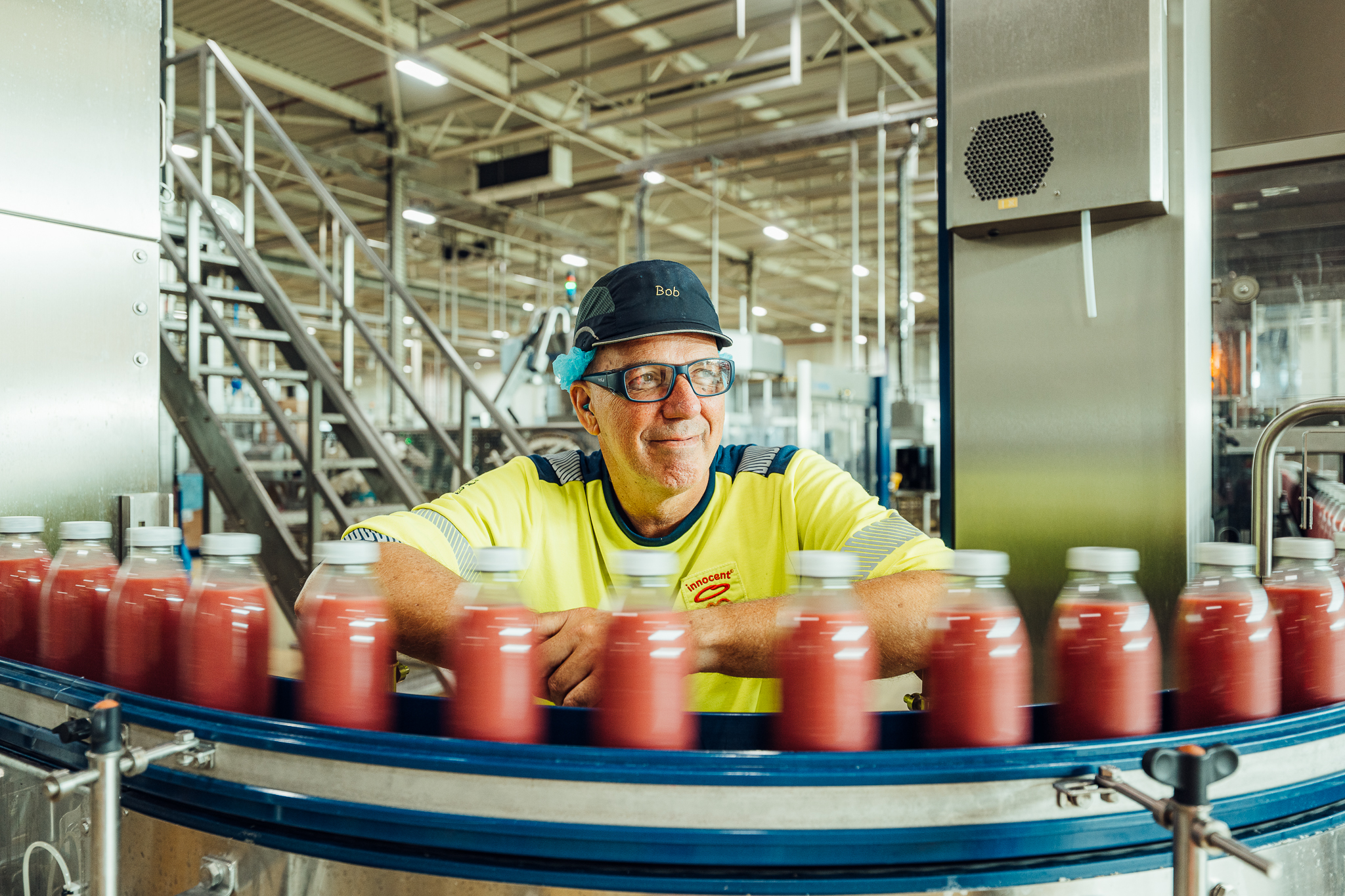Man watching juice bottles on conveyor belt. Bob's hat.
