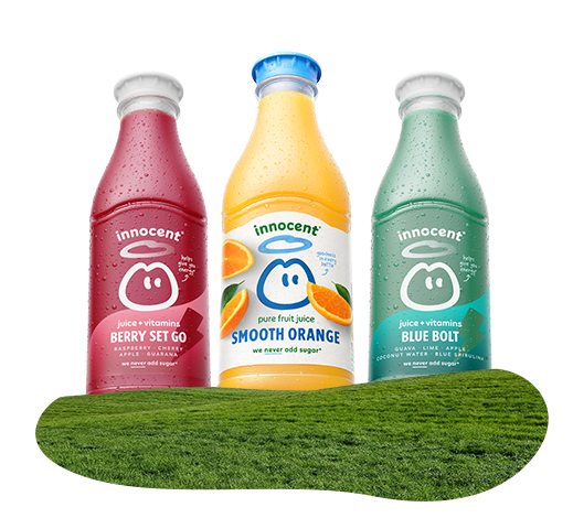 Three Innocent smoothie bottles on a grassy surface.